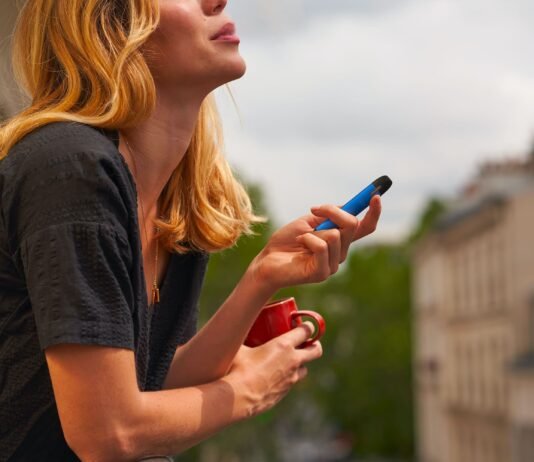 E-Zigarette im Urlaub – Das gilt es zu beachten Frau raucht E-Zigarette auf dem Balkon im Urlaub