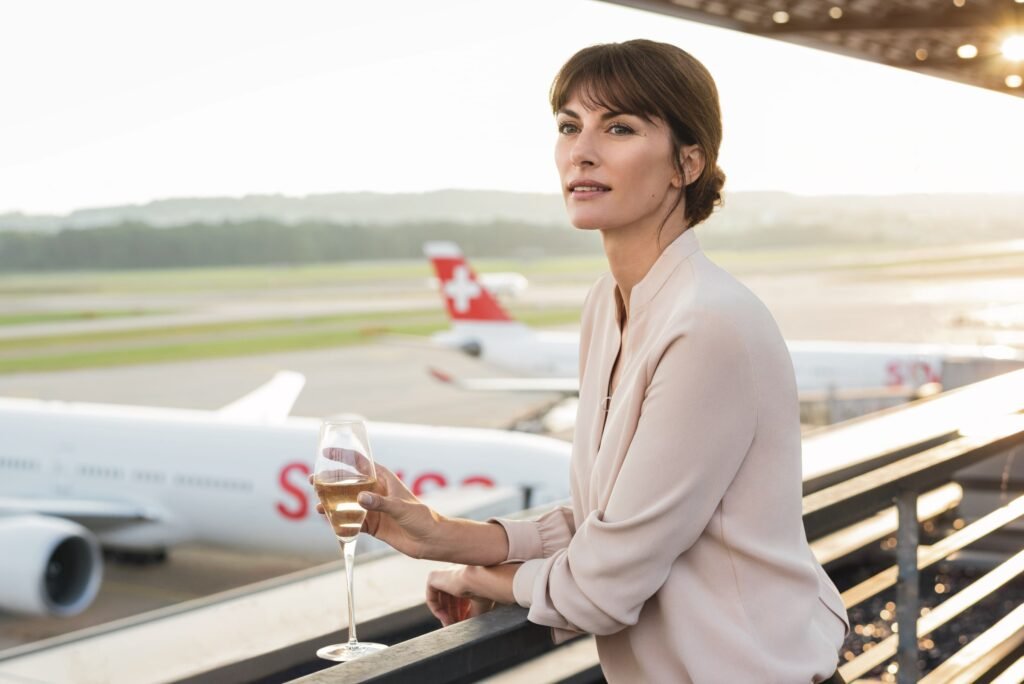 Frau trinkt Wein in der Lounge mit Blick auf die Landebahn des Flughafens